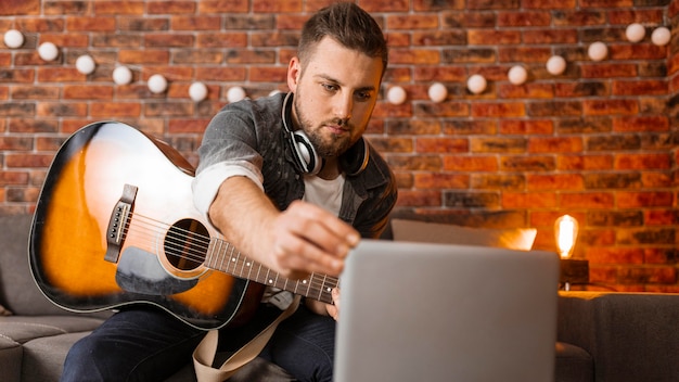 Hombre de tiro medio con guitarra y portátil