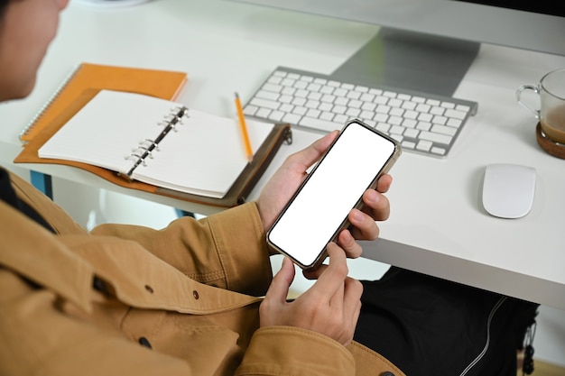 Hombre de tiro recortada con teléfono inteligente mientras está sentado en su lugar de trabajo.