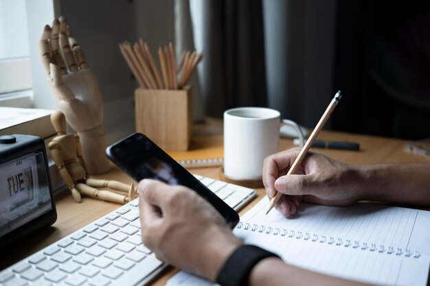 Hombre de tiro recortado usando teléfono móvil y tomando nota en el cuaderno