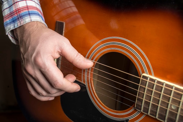 Un hombre toca la guitarra, primer plano que muestra los dedos punteando las cuerdas.