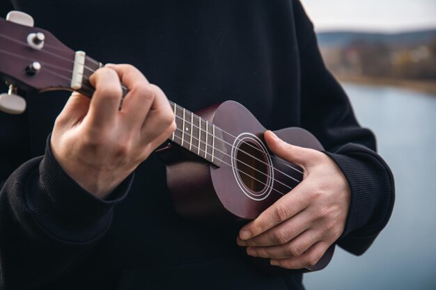 Un hombre toca la guitarra ukelele en el primer plano de la naturaleza de su mano