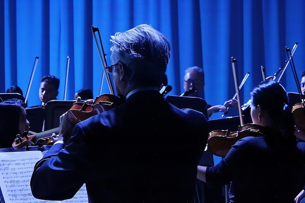 un hombre toca el violín frente a un escenario con otros músicos