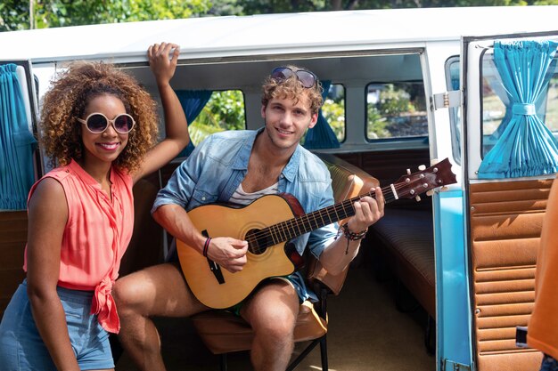 Hombre tocando la guitarra en autocaravana y mujer de pie junto a él