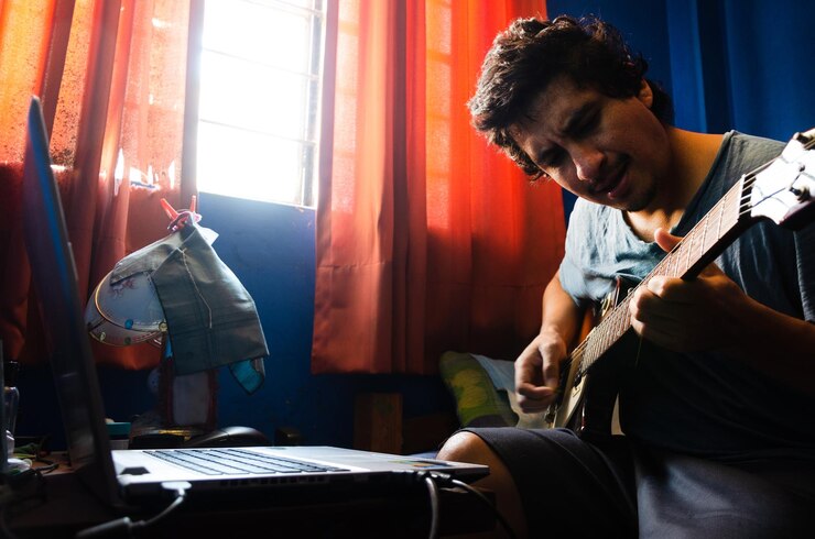 Foto hombre tocando la guitarra por computadora portátil en la mesa en casa
