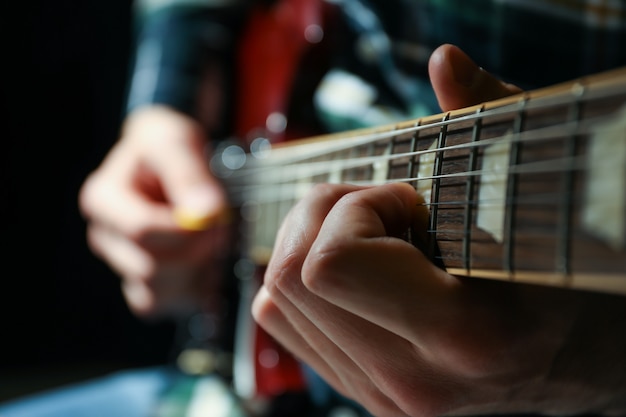 Foto hombre tocando la guitarra eléctrica contra el fondo oscuro, primer plano