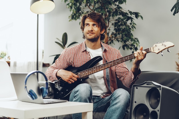 Hombre tocando la guitarra eléctrica y grabando música en un portátil