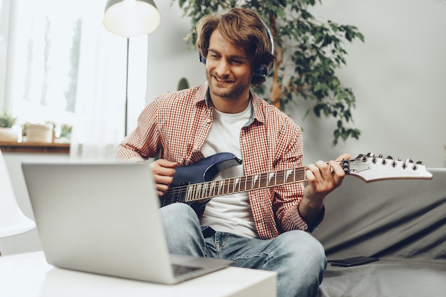 Hombre tocando la guitarra eléctrica y grabando música en un portátil