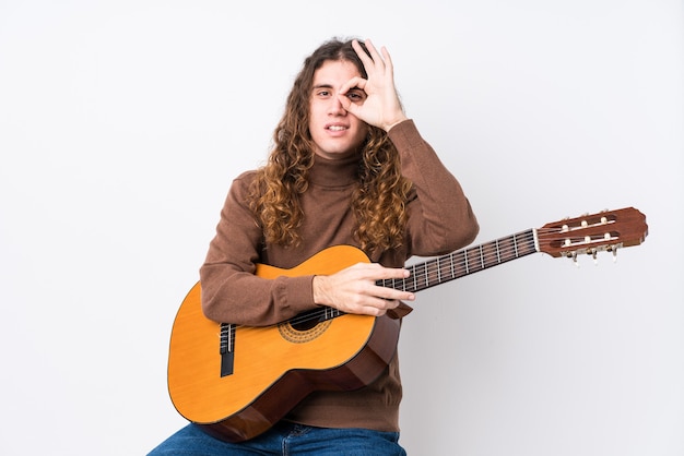 Hombre tocando la guitarra con gesto ok en el ojo