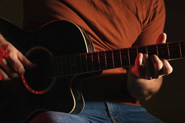 Hombre tocando la guitarra con luz de neón. Persona irreconocible ensayando. Rasgueo de guitarra acústica.