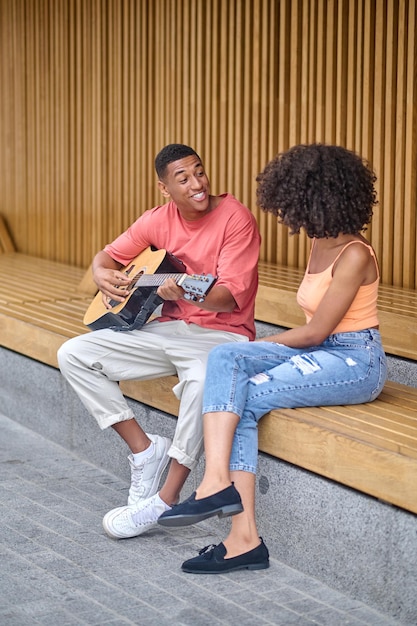 Hombre tocando la guitarra y mujer escuchando sentados al aire libre