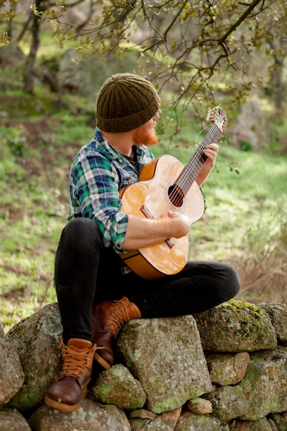 Foto hombre tocando la guitarra en la roca