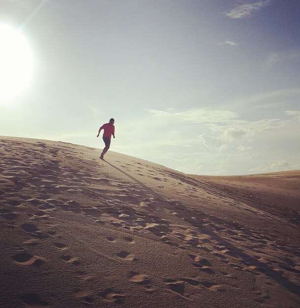 Foto hombre de toda la longitud en la arena en la playa contra el cielo