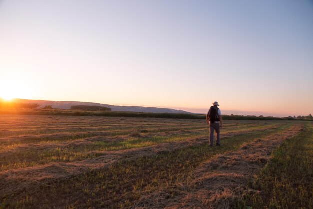 Hombre de toda la longitud caminando por el campo contra el cielo durante la puesta de sol