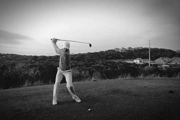 Foto hombre de toda la longitud jugando al golf en el campo contra el cielo