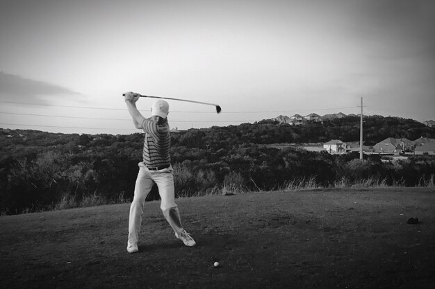 Hombre de toda la longitud jugando al golf en el campo contra el cielo