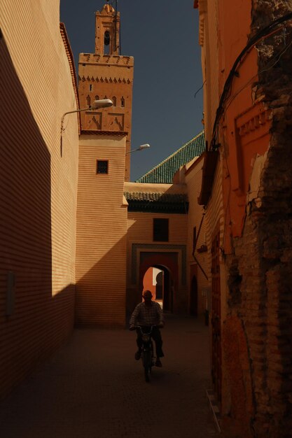 Foto hombre de toda la longitud montando una bicicleta en un callejón en medio de edificios en la ciudad