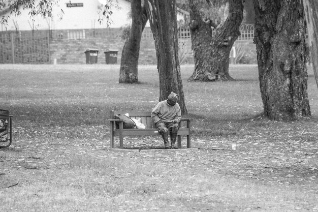 Foto hombre de toda la longitud sentado en un banco en el parque