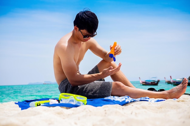 Hombre de toda la longitud usando loción protectora solar mientras está sentado en la playa