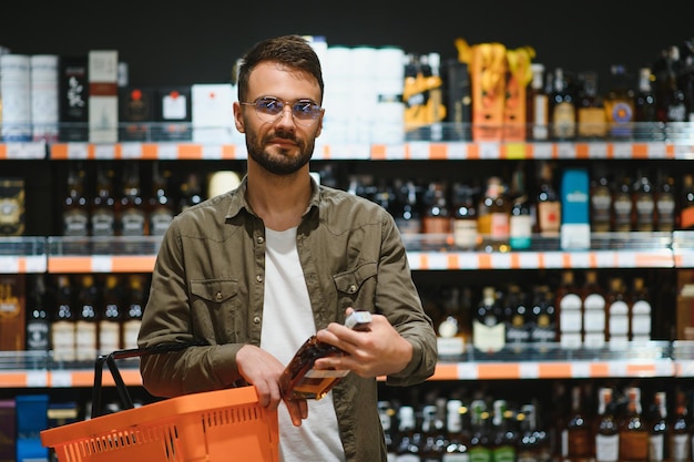 Un hombre toma bebidas alcohólicas del estante del supermercado Comprando alcohol en la tienda