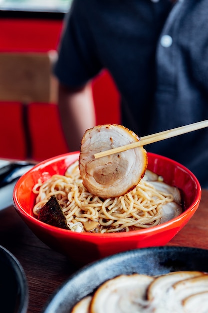 El hombre toma el cerdo Chashu del tazón con los palillos de Shoyu Chashu Ramen de la mano.