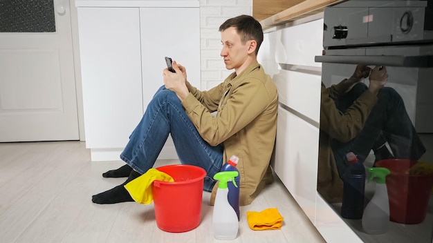 El hombre toma un descanso después de limpiar la cocina usando el teléfono móvil