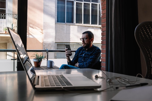 El hombre se toma un descanso del teletrabajo mirando su teléfono inteligente