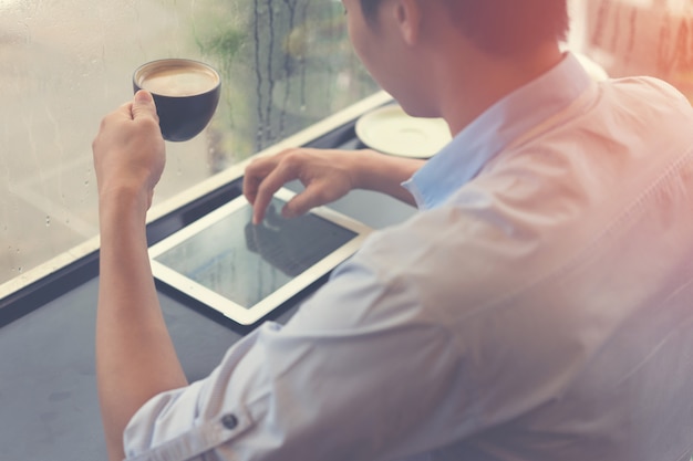 Hombre tomando café y usando la tableta en la cafetería con relajación