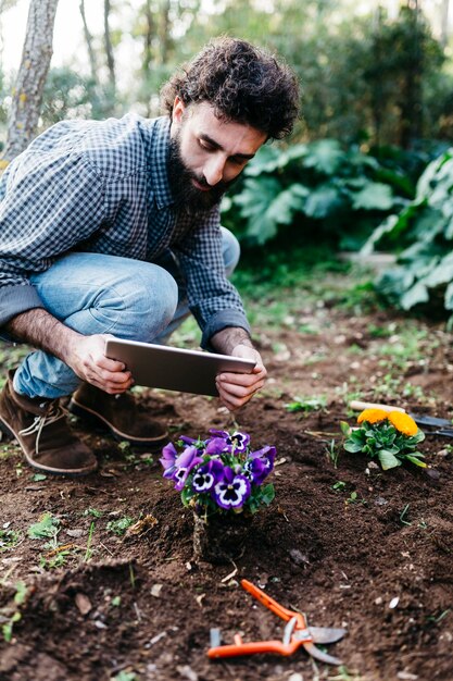Foto hombre tomando fotografías con una tableta de flores plantadas en el jardín
