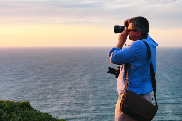 Hombre tomando fotos de la puesta de sol sobre el mar Mediterráneo en Portoscuso, Carbonia-Iglesias, Cerdeña, Italia