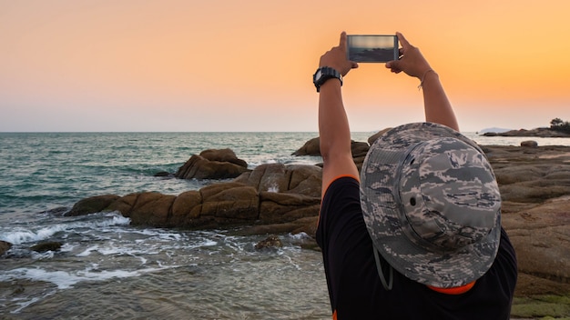 Hombre tomando fotos de la puesta de sol con teléfono móvil.