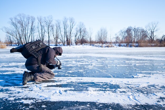 Hombre tomando fotos río cubierto de hielo y nieve