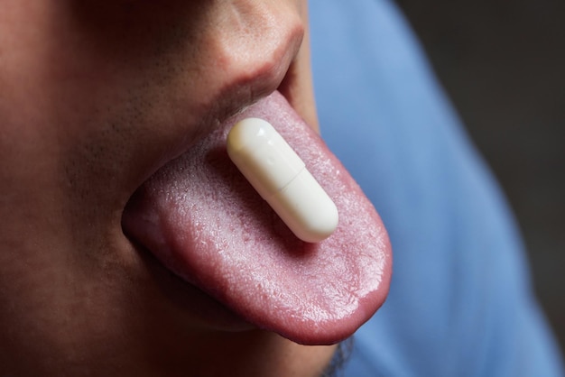 Hombre tomando pastillas con la boca abierta y la lengua fuera