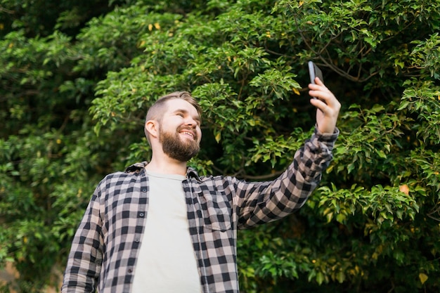 Hombre tomando selfie retrato sobre fondo de árbol feliz millennial guy disfrutando de las vacaciones de verano en cit