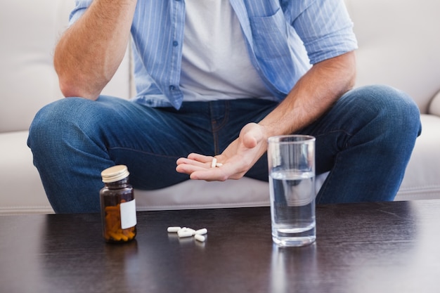 Hombre tomando sus pastillas en el sofá