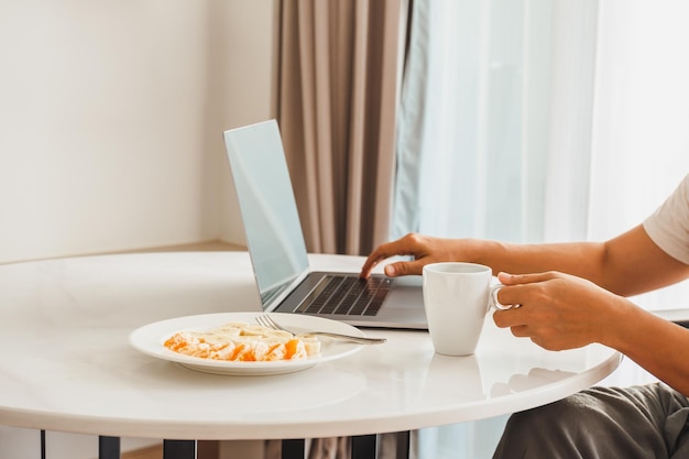 Hombre tomando una taza de café con frutas frescas mientras trabaja en una computadora portátil