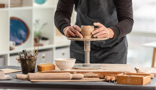 Hombre con torno de alfarería para moldear la taza de arcilla en el taller