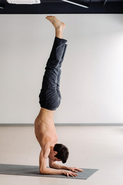 Foto un hombre con un torso huesudo entrena de pie sobre sus manos en el gimnasio.