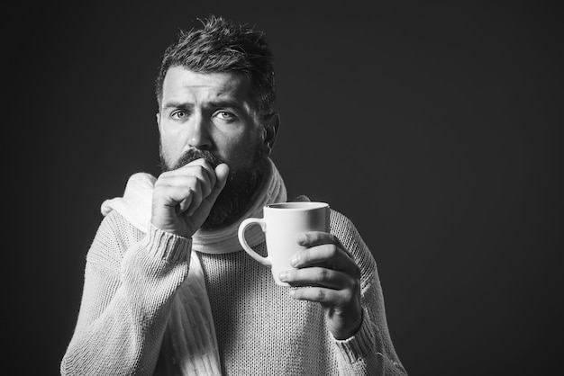 Hombre tosiendo en su mano hombre barbudo está tosiendo porque tiene gripe y bebe té caliente de la taza