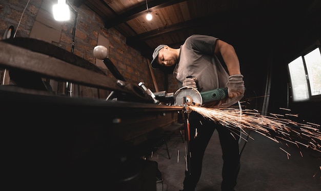 Un hombre trabaja con una amoladora angular en el taller de su casa Fabricación de productos metálicos con sus propias manos