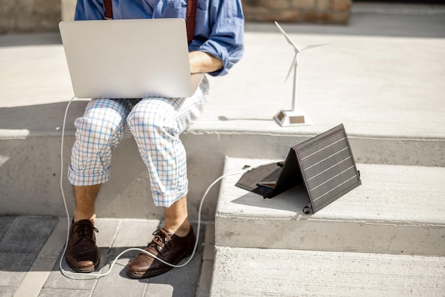 El hombre trabaja y carga la computadora portátil desde el panel solar portátil