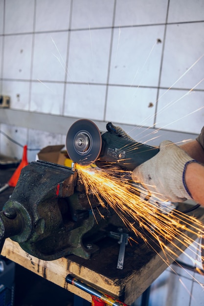 Foto un hombre trabaja como molinero en un taller un maestro en gafas molina una parte sujetada en un tornillo con un molinero chispas del metal vuelan alrededor como una fuente brillante