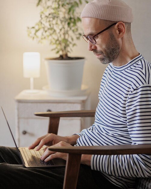 El hombre trabaja en una computadora portátil en casa, un diseñador independiente o un alto gerente trabaja en línea o ve un