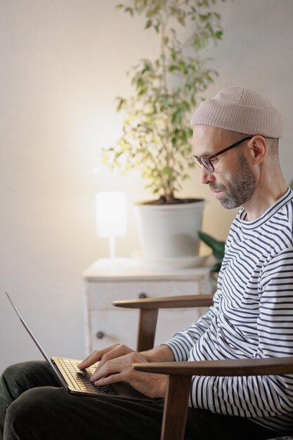 El hombre trabaja en una computadora portátil en casa, un diseñador independiente o un alto gerente trabaja en línea o ve un