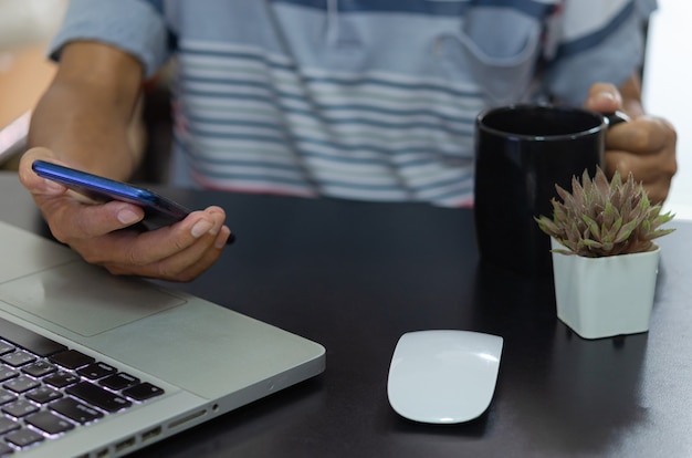 El hombre trabaja en una computadora portátil que sostiene el teléfono móvil en línea y la cafetera funciona, concepto de cosas de Internet