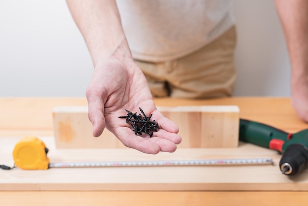 Un hombre trabaja con un destornillador eléctrico en una mesa de madera y también toma medidas con una cinta métrica