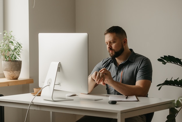 Un hombre trabaja de forma remota en una computadora de escritorio. Un tipo con barba desplaza su reloj inteligente durante una videoconferencia en casa. Un profesor se está preparando para una conferencia en línea.