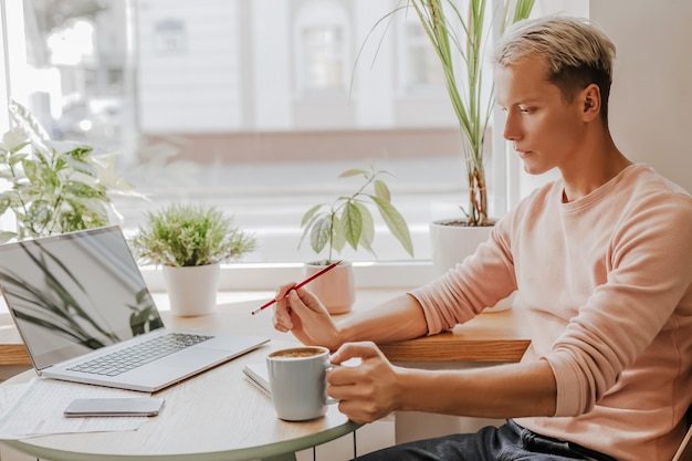 El hombre trabaja en el lugar de trabajo con documentos y bebe café en un café ecológico con plantas.