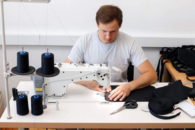 Un hombre trabaja en una máquina de coser en la producción de costura. sin género