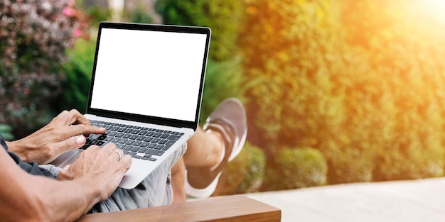 Un hombre trabaja en la naturaleza sentado en una silla con una laptop.