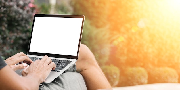 Un hombre trabaja en la naturaleza sentado en una silla con una laptop.